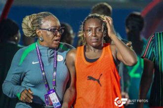 Female athlete in an orange jersey looks distressed as a coach with braided hair consoles her after a race in a sports venue. (Informative)