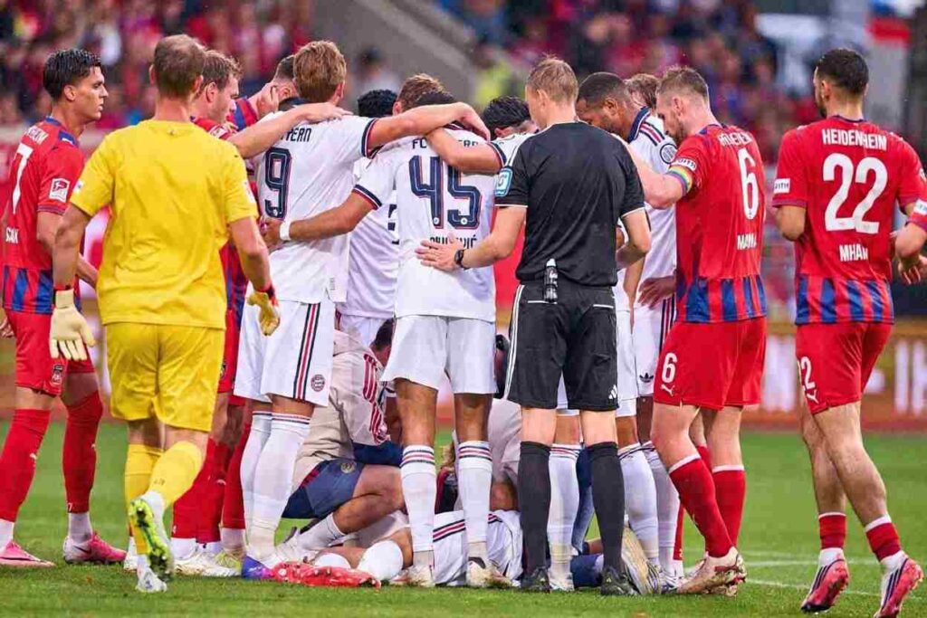 Bayern Munich Players Trybal News Bayern Munich midfielder Jamal Musiala receives treatment on the pitch from FC Bayern team doctor Prof Dr Peter Ueblacker after falling during a preseason friendly between 1 FC Heidenheim and FC Bayern Munich at Voith Arena on August 18 2026 in Heidenheim Germany Bayern players including Harry Kane 9 and Heidenheim players surround them trybalnews