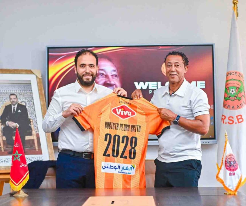 Two men in white shirts hold up an orange sports jersey labeled 2028 in a formal room setting smiling for the camera  trybalnews