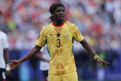 Ghana national football player in a yellow kit with number 3, arms outstretched on the field