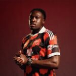 Portrait of a male soccer player wearing a red and black club jersey hands clasped against a dark red backdrop  trybalnews