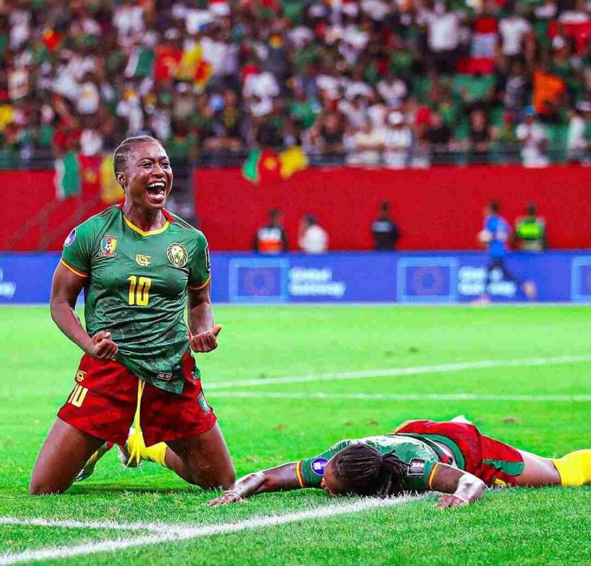 Cameroonian footballer wearing green jersey number 10 celebrates a goal on a green pitch with a fallen opponent nearby and a cheering crowd in the stands  trybalnews