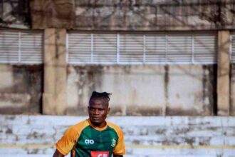 Male soccer player in green and orange kit performing an agility drill with orange cones on a training field.