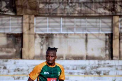 Male soccer player in green and orange kit performing an agility drill with orange cones on a training field.