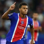 Soccer player in blue and red jersey points upward during a celebration on the field  trybalnews