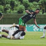 Soccer players in green and white chase the ball on a grass field one player tumbles as others move toward the ball  trybalnews