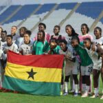 Ghana womens soccer team posing on the field with a Ghana flag in front of them on a stadium pitch  trybalnews