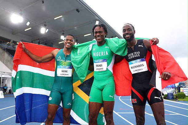IMG20260801WA0000 Trybal News Four male sprinters on a track each wrapped in his national flagSouth Africa Jamaica Nigeria and Trinidad and Tobagosmiling with arms around each other trybalnews