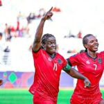 Three female soccer players in red jerseys celebrate on a green pitch arms raised in triumph with a blurred stadium crowd behind them  trybalnews