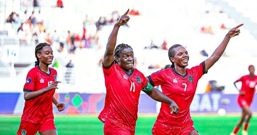 Three female soccer players in red jerseys celebrate on a green pitch arms raised in triumph with a blurred stadium crowd behind them  trybalnews