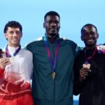 Gold medalist Ezekiel Nathaniel of Team Nigeria in green tracksuit stands on the podium with silver medalist Jake Minshull of Team England in red and white jacket on the left and bronze medalist Assinie Wilson of Team Jamaica in black tracksuit on the right during the Mens 400 Metres Hurdles Final medal ceremony on Day 8 of the Glasgow 2026 Commonwealth Games at Scotstoun Stadium July 31 2026  trybalnews
