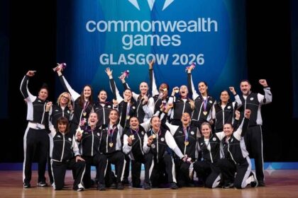 Gold medalists of Team New Zealand celebrate during the Netball medal ceremony on Day 10 of the Glasgow 2026 Commonwealth Games at The Hydro, August 2, 2026. Players and coaches in black and white tracksuits pose together on stage, holding up gold medals and Commonwealth Games mascots with a "Commonwealth Games GLASGOW 2026" backdrop behind them.
