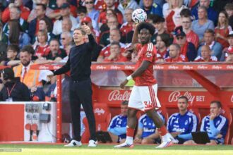 Nottingham Forest manager Oliver Glasner, left, in a black tracksuit gives instructions as player Ola Aina, wearing a red home kit, prepares to take a throw-in during a Premier League match at the City Ground in Nottingham on Saturday August 22, 2026