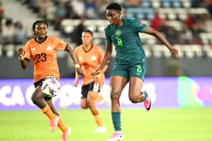 Two female soccer players chase the ball during a match; green Nigeria kit (#8) vs orange kit (#23).