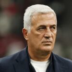 Older man with silver hair wearing a dark blazer and white shirt looking to the side with a blurred stadium crowd in the background  trybalnews