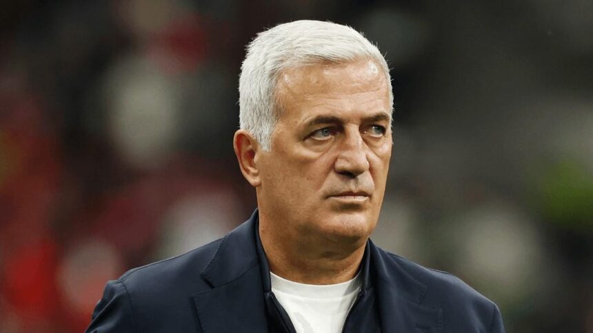 Older man with silver hair wearing a dark blazer and white shirt looking to the side with a blurred stadium crowd in the background  trybalnews