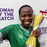 Smiling female athlete in a green jersey holds a gold trophy at a Woman of the Match event backdrop  trybalnews