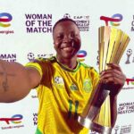 Female soccer player in a yellow jersey posing with a tall gold trophy smiling against a Woman of the Match backdrop  trybalnews