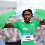 Nigerian sprinter crosses the finish line with arms raised draped in a green and white Nigerian flag  trybalnews