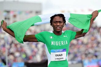Nigerian sprinter crosses the finish line with arms raised, draped in a green and white Nigerian flag.