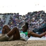 Female track and field athlete lands in the sand pit during a long jump arms extended with a crowded stadium in the background  trybalnews