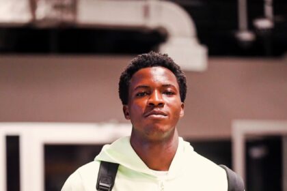 Portrait of a young man wearing a mint-green hoodie with a backpack indoors, looking at the camera.