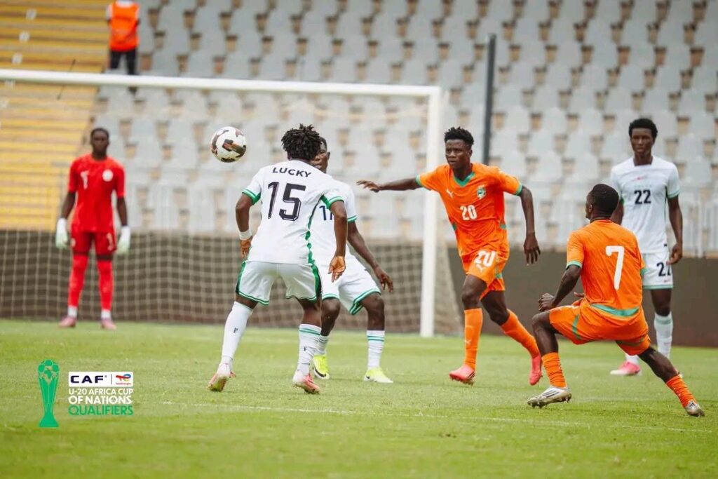 Flying Eagles Trybal News Soccer players in white and orange compete for the ball near the goal with a red jersey goalkeeper in the background CAF U 20 Africa Cup logo in corner trybalnews
