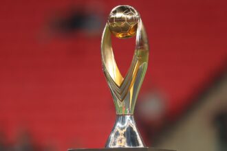 Golden trophy with a spherical top and curved arms on a square base against a red blurred background.