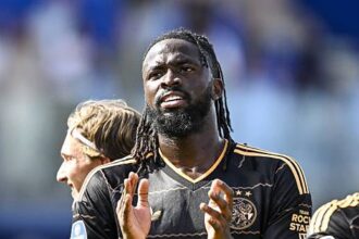 African soccer player in a black Ziggo jersey claps on the field during a match.