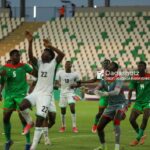 Soccer match with players in white and green jerseys contesting the ball on a green field empty stadium seating in the background  trybalnews