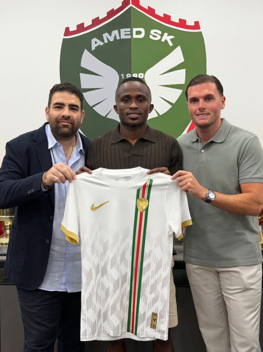Three men pose holding a white soccer jersey with a gold Nike swoosh and a greenredgreen vertical stripe in front of a club crest  trybalnews