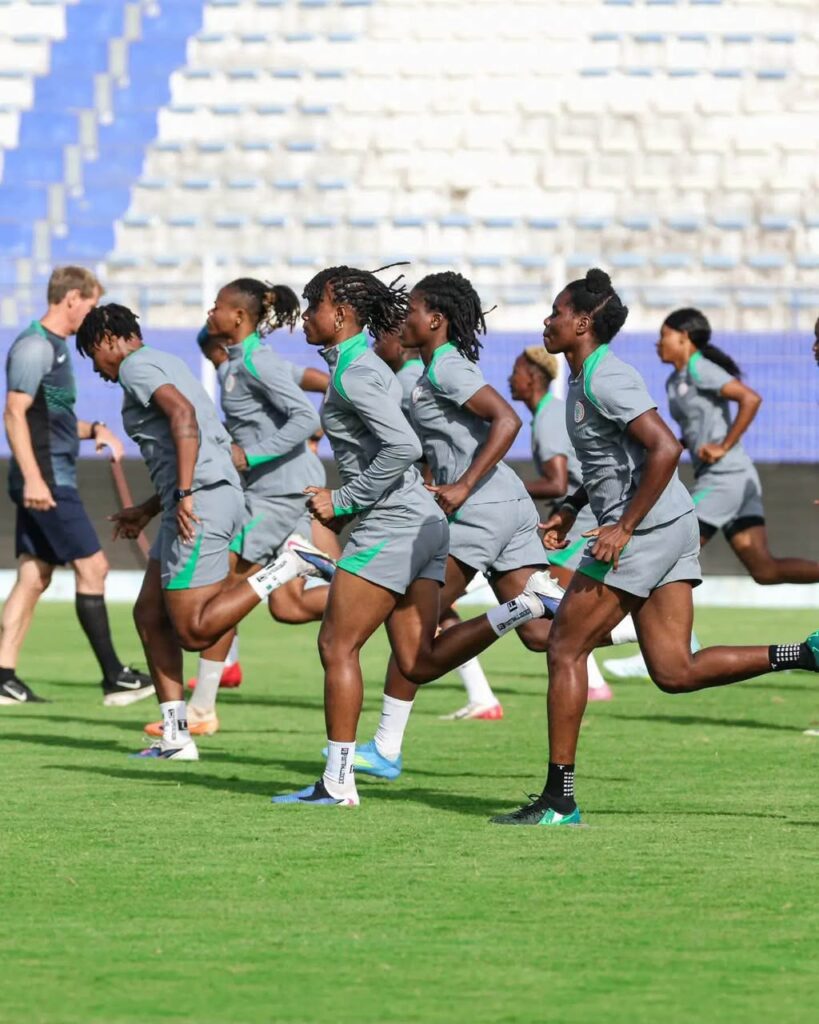 Soccer players in gray training kits sprinting on a green field during a practice session with empty stadium seats in the background  trybalnews