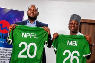 Two men hold up green sports jerseys with numbers 20 and 26, symbolizing team players during a signing/press event.