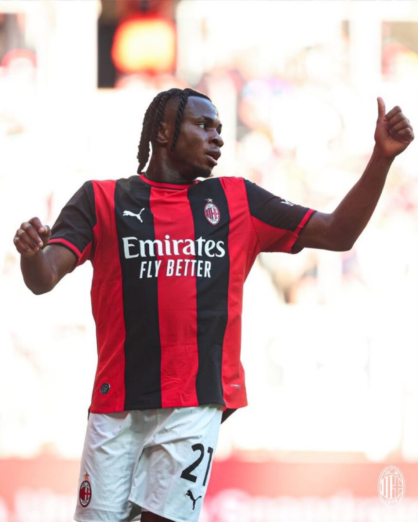 Soccer player in AC Milan red and black jersey celebrating with arm raised and thumbs up on the pitch  trybalnews