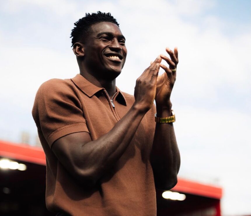Man smiling and clapping outdoors wearing a brown polo shirt and gold watch  trybalnews