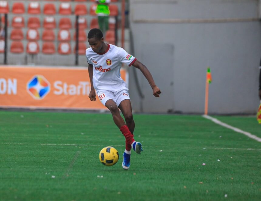 Soccer player in a white kit with red trim dribbling a yellow ball on a green field during a match  trybalnews
