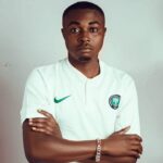 Portrait of a young man with short hair arms crossed wearing a white soccer jersey with a green Nike swoosh and a club badge on the chest  trybalnews