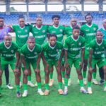 Group of soccer players in green uniforms posing for a team photo on a field with empty blue stadium seats in the background  trybalnews