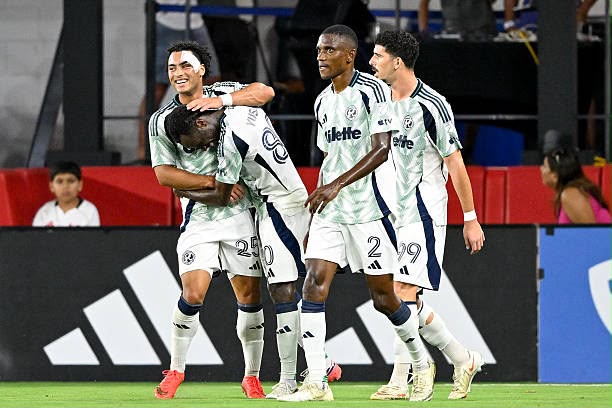 Alhassan Yusuf Trybal News Four soccer players in light green jerseys celebrate a goal on the pitch with one teammate embracing another in a hug while others smile and walk together trybalnews