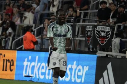 Soccer player in a mint-green jersey (number 88) celebrating on the field with fans in the stands behind him.