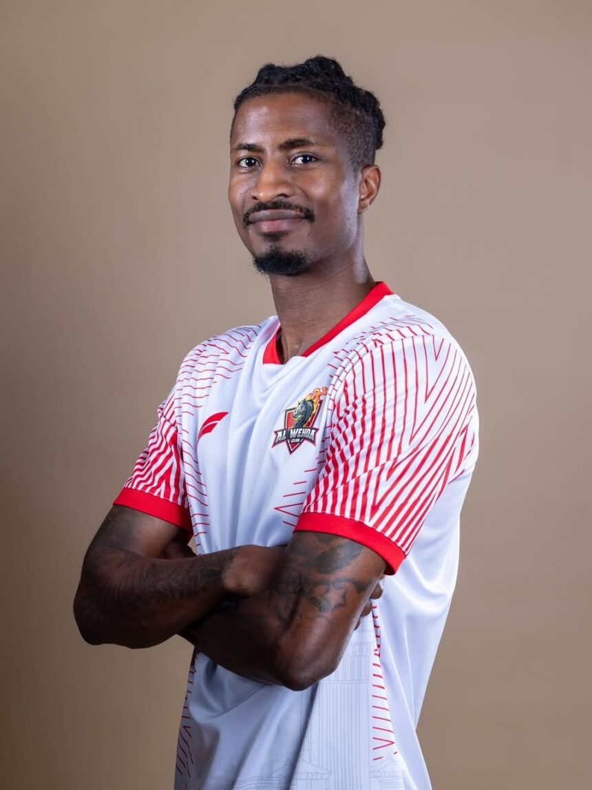 Portrait of a man with short dreadlocks wearing a white and red sports jersey arms crossed smiling slightly against a neutral backdrop looking at the camera  trybalnews