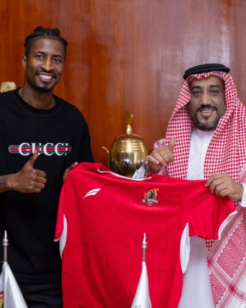 Two men smile and hold up a red team jersey with a trophy on a wooden wall behind them  trybalnews