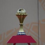 The Africa Cup of Nations trophy displayed on a red pedestal before the AFCON final between Morocco and Senegal at Complexe Sportif Prince Moulay Abdellah in Rabat Morocco on January 19 2026 The gold trophy features a globe of Africa on top and CAF on the stem  trybalnews