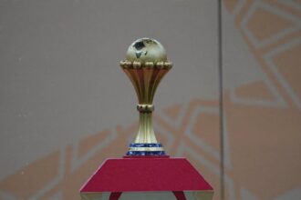 The Africa Cup of Nations trophy displayed on a red pedestal before the AFCON final between Morocco and Senegal at Complexe Sportif Prince Moulay Abdellah in Rabat, Morocco on January 19, 2026. The gold trophy features a globe of Africa on top and "CAF" on the stem.