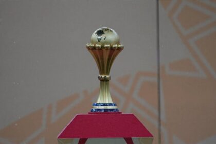 The Africa Cup of Nations trophy displayed on a red pedestal before the AFCON final between Morocco and Senegal at Complexe Sportif Prince Moulay Abdellah in Rabat, Morocco on January 19, 2026. The gold trophy features a globe of Africa on top and "CAF" on the stem.