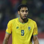 Gabon forward Pierre Emerick Aubameyang reacts during the Africa Cup of Nations Group F match between Cameroon and Gabon at Adrar Stadium in Agadir on December 24 2025 The striker wears Gabons yellow home jersey with blue number 9 and the FEGAFOOT crest with a blurred stadium crowd in the background  trybalnews