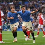 Brighton  Hove Albion midfielder Chema Andres wearing a blue shirt and number 14 shorts celebrates with teammate Luka Vuskovic after scoring both with arms extended and pointing Arsenal defender J Timber in red and white number 12 kit stands nearby on the pitch at the American Express Stadium  trybalnews