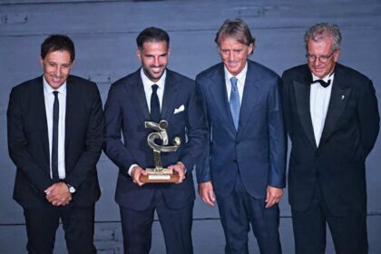 Como’s Spanish coach Cesc Fabregas, second from left, smiles while holding the AIC Coach of the Year award trophy. He poses next to Italy national team head coach Roberto Mancini, second from right, at the Italian Footballers' Association gala and awards ceremony at La Scala Theatre in Milan, Italy on September 2, 2026. All four men are in suits on a blue stage backdrop.
