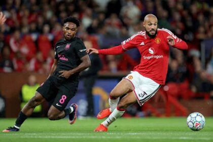 Christian Nwachukwu of Sabah FC in a black jersey with pink number 8 challenges Noussair Mazraoui of Manchester United in a red home kit during the UEFA Champions League 2026/27 League Phase match at Old Trafford on September 10, 2026 in Manchester, England.