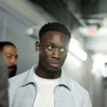 USMNT forward Folarin Balogun of the United States arrives at Fanatics Fest at Javits Center in New York New York on July 17 2026 ahead of a press conference for the FIFA World Cup 2026 Final He wears a light blue striped shirt over a white t shirt and a diamond earring walking through a hallway with other people in the background  trybalnews